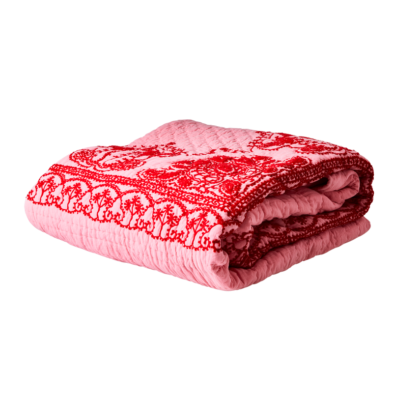 A pink blanket with red floral embroidery.